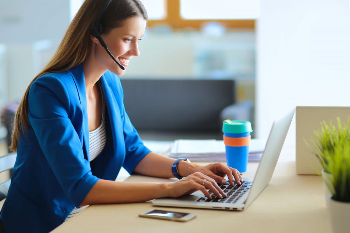 Portrait of beautiful business woman working at her desk with headset and laptop.